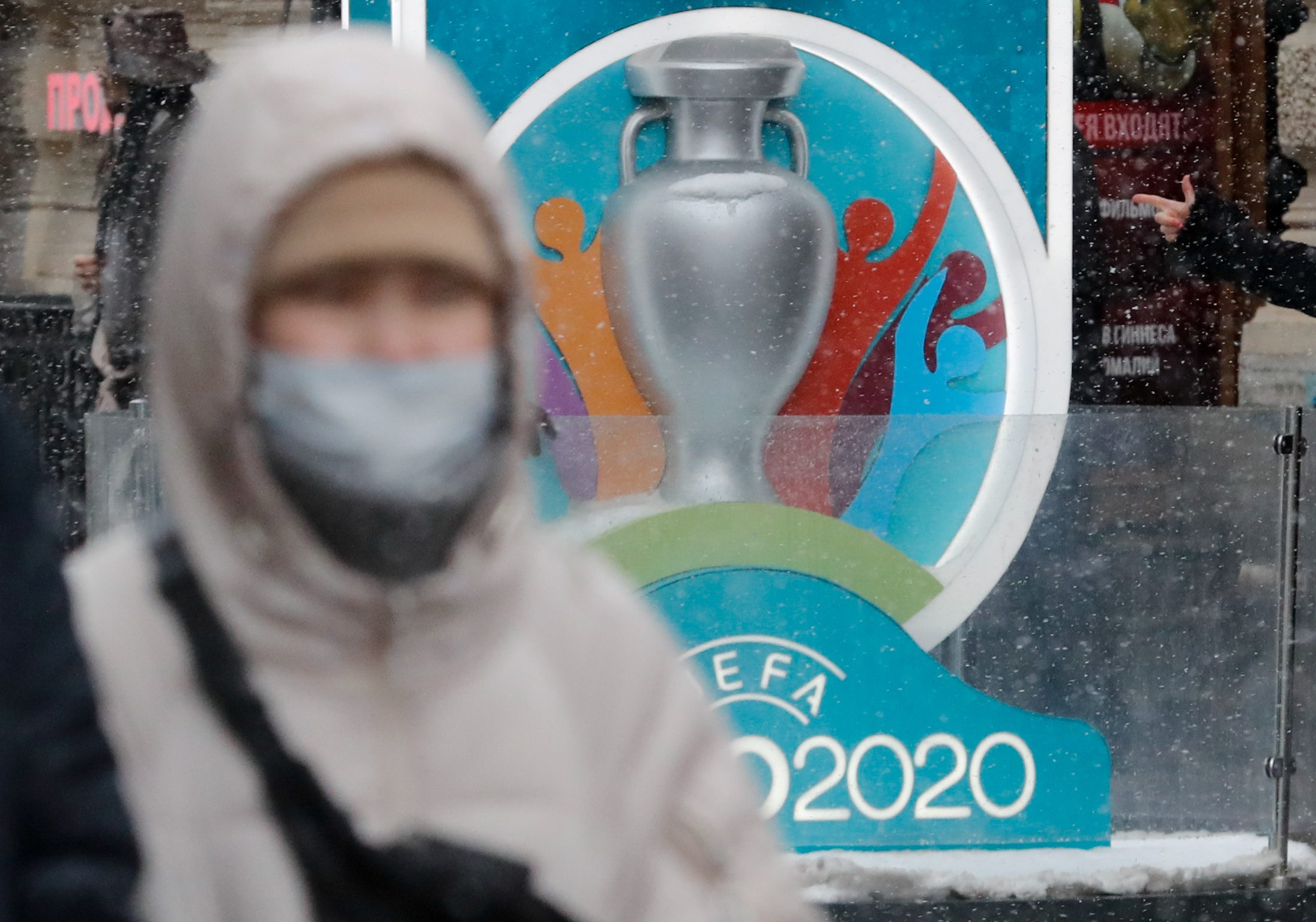 مواطن روسي يرتدي قناعاً ويمر بجانب أحد إعلانات بطولة "يورو 2020" في سان بطرسبرغ (رويترز)